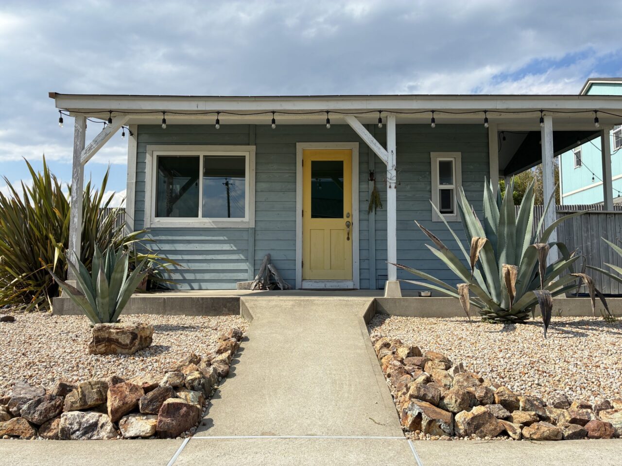 Sunny Sunday Nailの外観写真。ブルーグレーの平屋で黄色いドアが特徴。